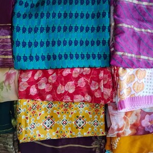 May include: A collection of folded fabric pieces featuring diverse patterns and colours. Visible designs include a teal leaf print, a red leaf pattern, a yellow geometric motif, and various floral prints in shades of purple, pink, and gold.