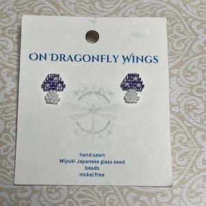 May include: A pair of mushroom-shaped earrings made with purple and white Miyuki Japanese glass seed beads. The earrings are hand sewn and nickel-free. The card reads "ON DRAGONFLY WINGS".