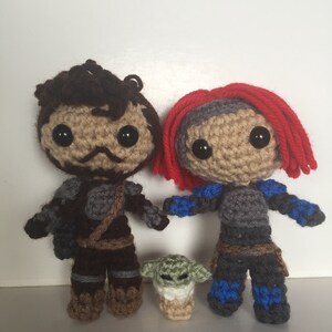 May include: Crocheted figures of two characters from the Star Wars franchise, one with brown hair and the other with red hair, standing next to a small green crocheted figure of a character from the same franchise.