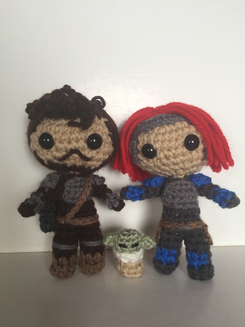 May include: Crocheted figures of two characters from the Star Wars franchise, one with brown hair and the other with red hair, standing next to a small green crocheted figure of a character from the same franchise.