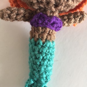 May include: Crocheted mermaid doll with brown hair, a purple top, and a teal tail.