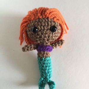 May include: Crocheted mermaid doll with brown skin, orange hair, purple top, and a teal tail.