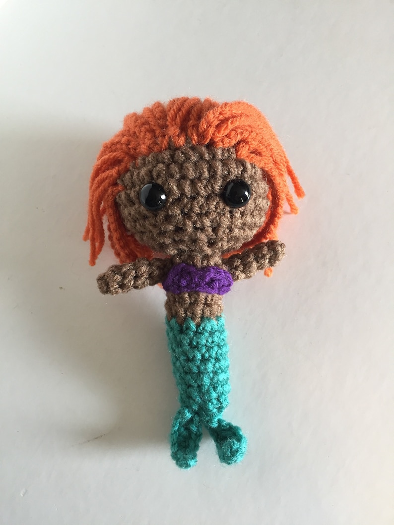 May include: Crocheted mermaid doll with brown skin, orange hair, purple top, and a teal tail.