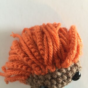 May include: A crocheted mermaid doll with brown skin, orange hair, and black eyes. The doll is wearing a turquoise and purple tail.