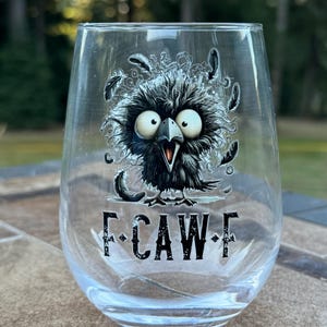 May include: A clear stemless wine glass with a cartoon crow illustration. The crow is black with large white eyes and an open beak. The text "F-CAW-F" is printed below the crow in black letters.