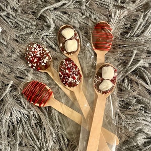 May include: Wooden spoons dipped in chocolate, decorated with red drizzle, crushed peppermint, and marshmallows. The spoons are packaged in a clear plastic bag, perfect for a sweet treat or hot cocoa.