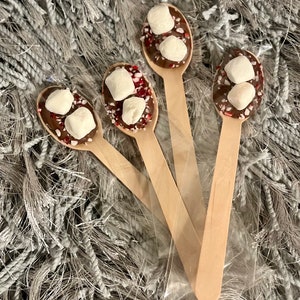 Puede incluir: Cuatro cucharas de madera con chocolate, malvaviscos y caramelos de menta triturados. Est&aacute;n empaquetadas en una bolsa de pl&aacute;stico transparente, sobre una superficie gris texturizada. Para chocolate caliente.