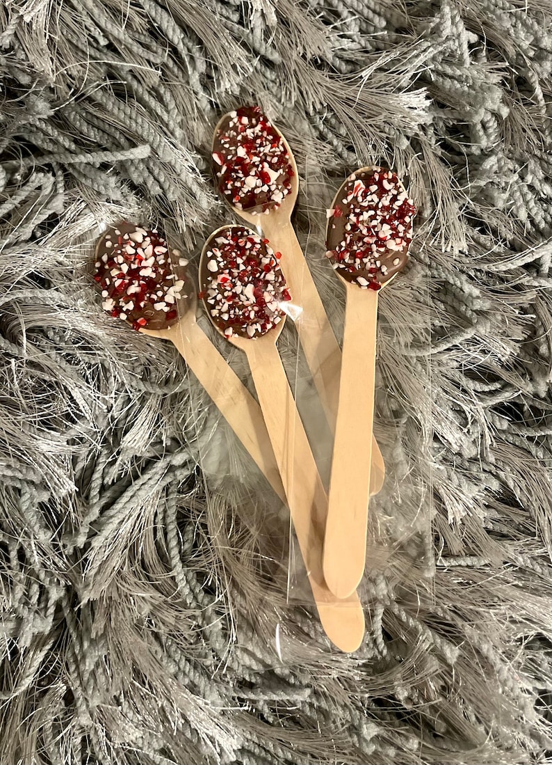 Puede incluir: Cuatro cucharas de madera con cobertura de chocolate y chispas rojas y blancas. Las cucharas est&aacute;n en una bolsa de pl&aacute;stico transparente. Fondo gris texturizado. Un dulce.