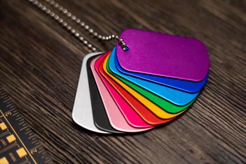 Puede incluir: Un conjunto de chapas de perro de metal de colores en una cadena plateada. Las chapas est&aacute;n dispuestas en forma de arco&iacute;ris, con la chapa superior de color morado y la inferior de color plateado.