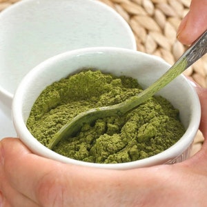 May include: A white ceramic bowl filled with a bright green powder, a silver spoon is partially submerged in the powder.