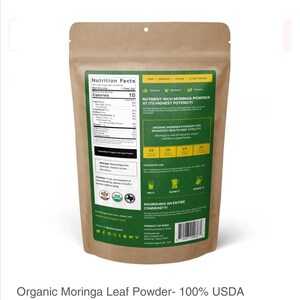 May include: A brown paper bag with a white label that says "Nutrition Facts" and lists the nutritional information for Organic Moringa Leaf Powder. The label also says "RAW, ORGANIC, VEGAN, PLANT BASED" and "NUTRIENT-RICH MORINGA POWDER AT ITS HIGHEST POTENCY!" The bag is sealed with a white sticker that says "USDA Organic".