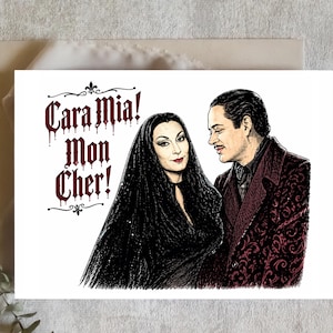 May include: Greeting card featuring a couple from The Addams Family. The illustration shows Morticia and Gomez Addams with the text "Cara Mia! Mon Cher!" in a gothic font. The card is on a neutral background.