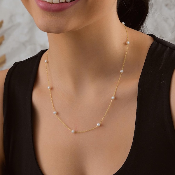 May include: A gold chain necklace with small white pearls. The necklace is worn by a person with dark hair and a black tank top.