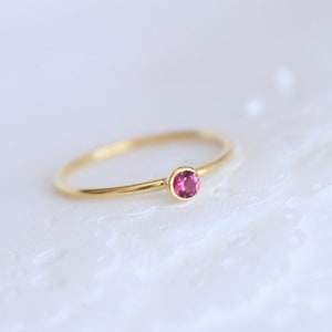 May include: A delicate gold ring with a single pink gemstone.
