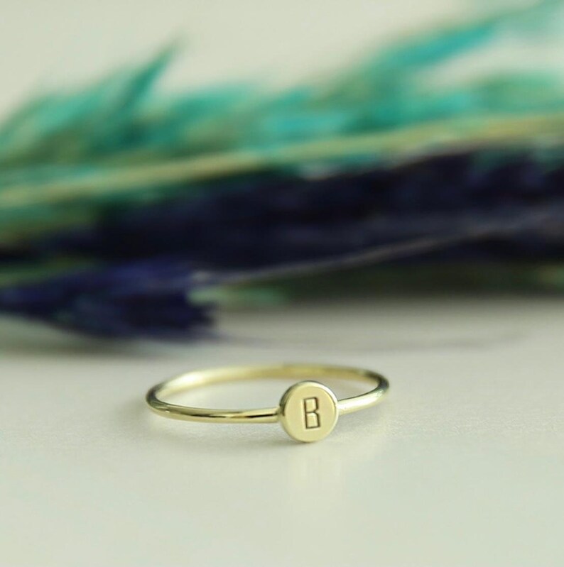May include: A gold ring with a round disc featuring the letter "B" engraved on it.