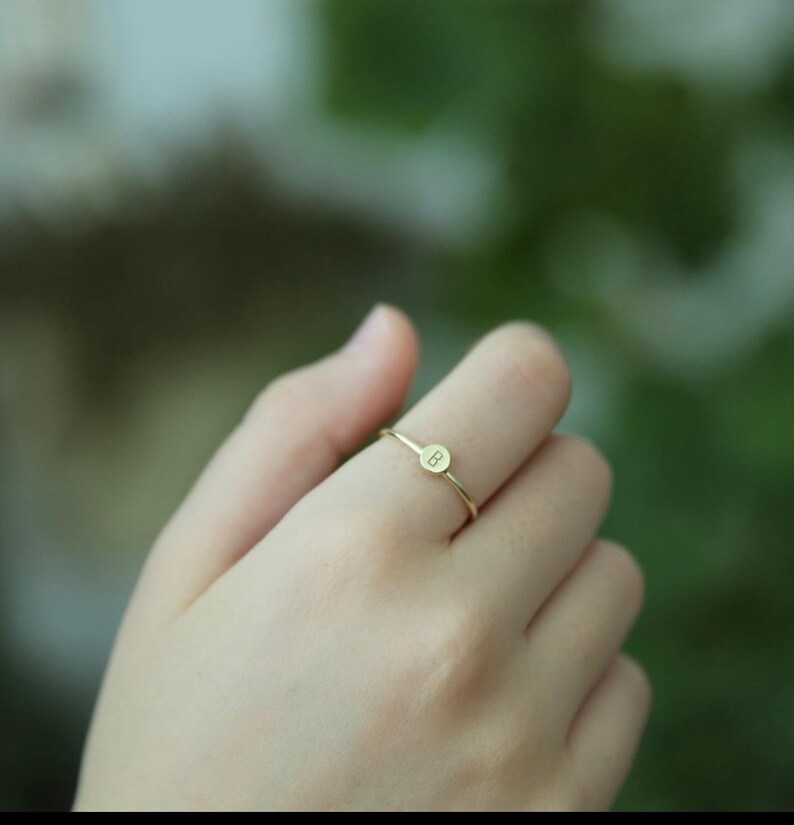 May include: A gold ring with a small round disc featuring the letter "B" engraved on it.