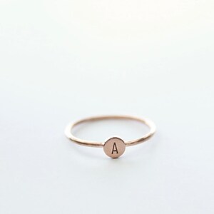 May include: A simple gold ring with a small round disc featuring the letter "A" engraved on it.