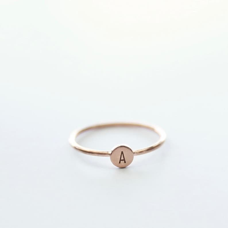 May include: A simple gold ring with a small round disc featuring the letter "A" engraved on it.