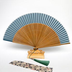 May include: A blue and brown folding fan with a decorative stand and a patterned fabric case. The fan is made of bamboo and has a tassel.