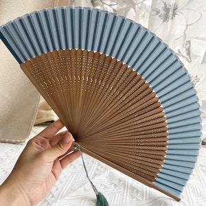 May include: A blue and brown folding fan with a green tassel. The fan is made of bamboo and has a delicate design.