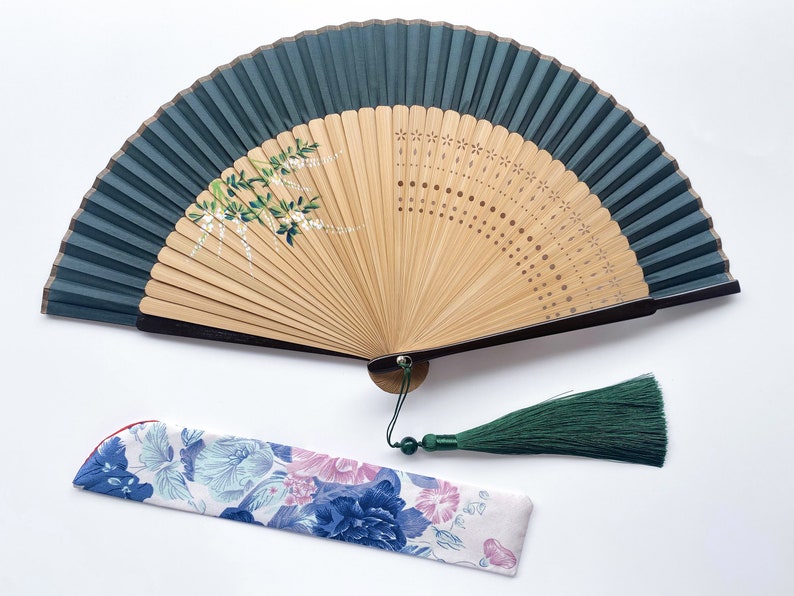 May include: A green and brown folding fan with a floral design and a green tassel. The fan is closed and has a floral patterned fabric case.
