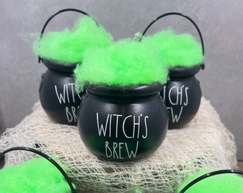 May include: Three black cauldron-shaped containers with green fuzzy material inside. Each container has a handle and the text "Witch's Brew" written in white on the front.