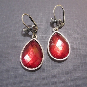 May include: A pair of silver dangle earrings with red teardrop-shaped crystals. The earrings have a lever back closure.
