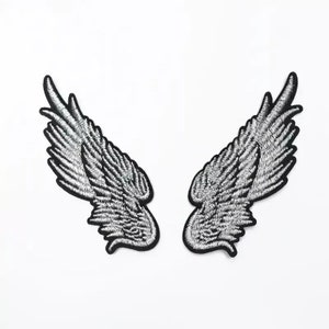 May include: A pair of silver embroidered angel wings with black outlines. The wings are separated and facing outwards.