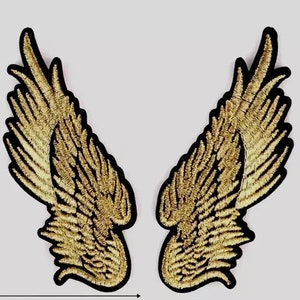 May include: A pair of gold embroidered angel wings with black outlines. The wings are separated and facing outwards.
