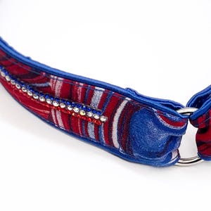 Könnte beinhalten: Nahaufnahme eines blau, rot und weiß gemusterten Halsbands mit einem silbernen Metallring. Das Halsband ist mit einer Reihe klarer und blauer Strasssteine verziert. Der Stoff hat ein patriotisches Design.