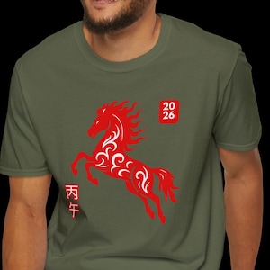 Puede incluir: Camiseta verde oliva con un diseño de caballo estilizado en rojo, los números "20 26" y caracteres chinos. La camiseta está hecha de un material suave y es adecuada para ropa casual.