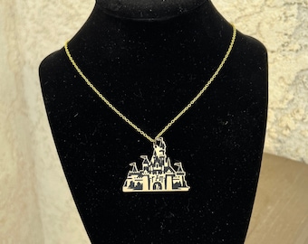 May include: A gold chain necklace with a black silhouette of a castle pendant.