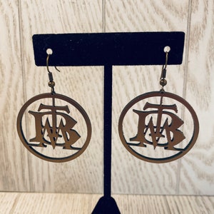 Puede incluir: Un par de pendientes de madera con un diseño circular. Los pendientes son marrones y presentan las letras "FWB" en una fuente estilizada.