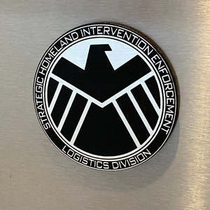 May include: A black and white round magnet with the text "Strategic Homeland Intervention Enforcement Logistics Division" and a shield logo in the center.