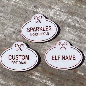May include: Three white oval-shaped name tags with red candy cane designs. The top tag reads "Sparkles North Pole". The middle tag reads "Custom Optional". The bottom tag reads "Elf Name".