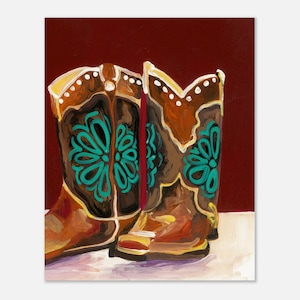 Op de afbeelding: Een schilderij van twee bruine cowboylaarzen met een turquoise bloemenontwerp. De laarzen staan tegen een dieprode achtergrond. De laarzen hebben een decoratieve rand met witte stippen.