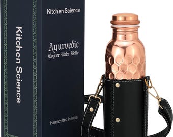 May include: A copper water bottle with a honeycomb design, in a black leather carrier with a shoulder strap. The bottle is next to a dark blue box with the text "Kitchen Science" and "Ayurvedic Copper Water Bottle".