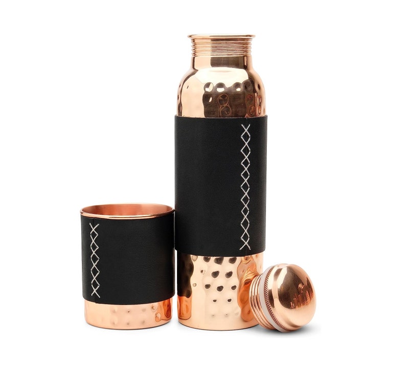 Puede incluir: Un juego de dos botellas de agua de cobre con fundas de cuero negro y costuras blancas. Las botellas tienen un acabado martillado y vienen con una tapa.