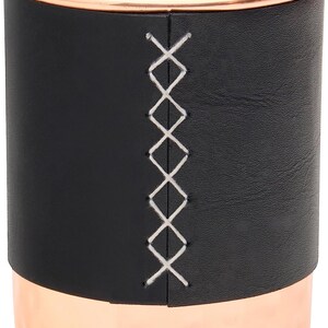 Puede incluir: Un vaso de cuero negro con borde de cobre y un dise&ntilde;o cosido blanco. El vaso es perfecto para guardar bol&iacute;grafos, l&aacute;pices u otros objetos peque&ntilde;os.