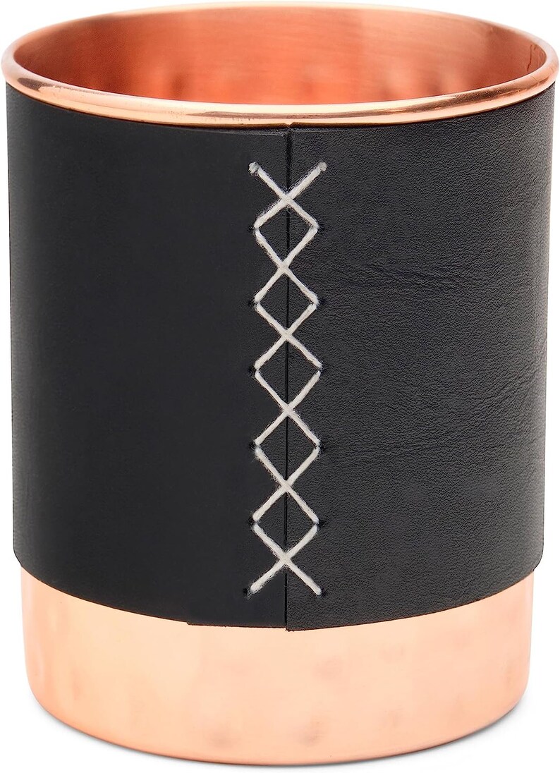 Puede incluir: Un vaso de cuero negro con borde de cobre y un dise&ntilde;o cosido blanco. El vaso es perfecto para guardar bol&iacute;grafos, l&aacute;pices u otros objetos peque&ntilde;os.