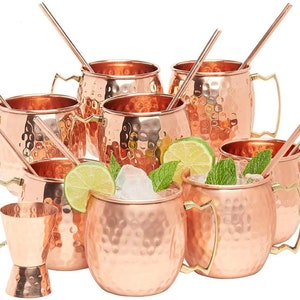 Puede incluir: Juego de ocho jarras de cobre martillado para Moscow Mule con asas doradas y pajitas. Las jarras est&aacute;n llenas de hielo, gajos de lima y hojas de menta.