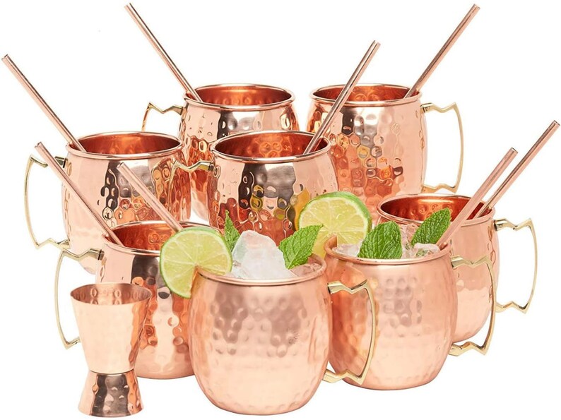 Puede incluir: Juego de ocho jarras de cobre martillado para Moscow Mule con asas doradas y pajitas. Las jarras est&aacute;n llenas de hielo, gajos de lima y hojas de menta.