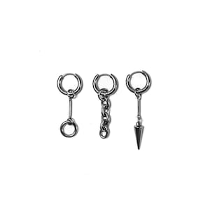 May include: Three silver-colored hoop earrings with different dangling charms. One earring has a small ring, another has a chain, and the third has a cone-shaped spike. The earrings are displayed against a white background.