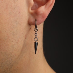 May include: A silver-toned earring with a conical pendant. The earring features a small hoop that connects to a series of small chain links, which then connect to the dark gray, cone-shaped pendant. The earring is shown against a dark background.