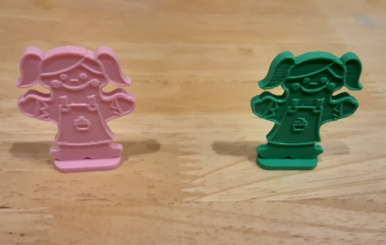 Pu&ograve; includere: Due figurine di plastica di ragazze con vestiti e codini. Una figurina &egrave; rosa e l'altra &egrave; verde.