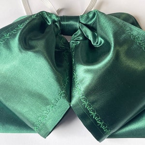 Peut inclure: Un nœud papillon en satin vert foncé avec un motif cousu décoratif sur les bords.