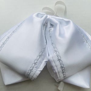 May include: A white satin bow tie with decorative gray stitching along the edges. The bow tie is tied with white ribbons. The item is likely for formal wear or special occasions.
