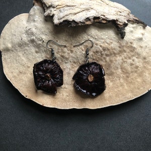 May include: Dark brown mushroom earrings with black metal hooks. The earrings have a unique, organic shape and texture, with a natural, earthy aesthetic. The earrings are displayed against a neutral background.