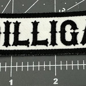 May include: Rectangular patch with the text "DILLIGAF" in bold, black, stylized letters on a white background. The patch has a black border. The patch is approximately 3 inches long.