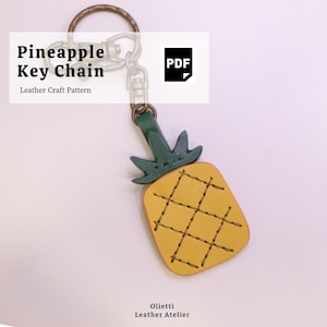 May include: A pineapple-shaped leather keychain with a yellow body and green top, featuring dark stitching in a cross-hatch pattern. The keychain is attached to a bronze-colored metal ring and clasp. Text reads: Pineapple Key Chain Leather Craft Pattern PDF.